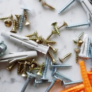 Bunch of various multicolored plastic dowels and metal screws placed on white marble table in modern workshop